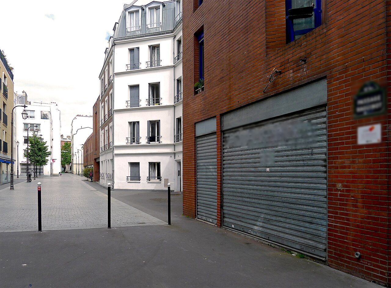 Rideaux métalliques baissés sur une façade en brique, dans un passage parisien.